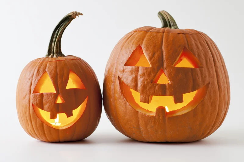 Two carved pumpkins with glowing faces side by side on white background
