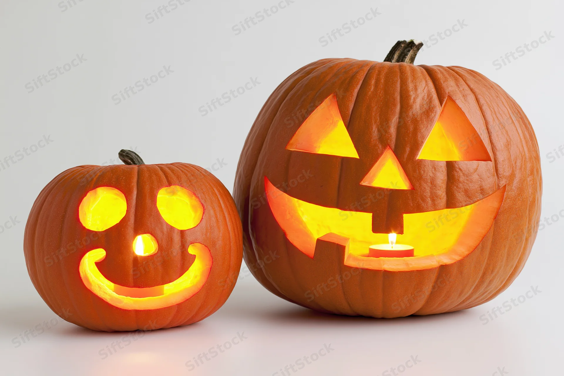 Two carved pumpkins with glowing faces side by side on white background