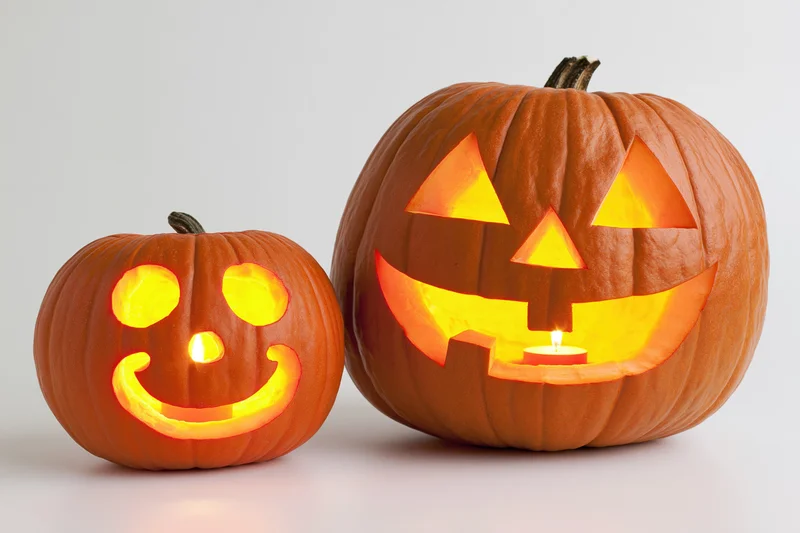 Two carved pumpkins with glowing faces side by side on white background