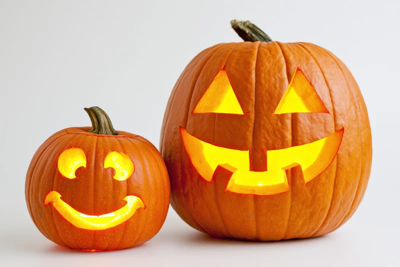 Two carved pumpkins glowing with smiling faces side by side on white background