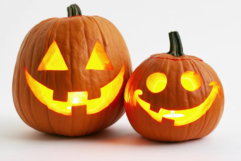 Two carved pumpkins with glowing faces side by side on white background