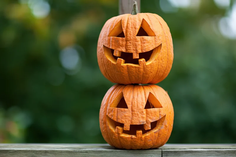 Two carved jack-o-lanterns stacked on a wooden surface outdoors