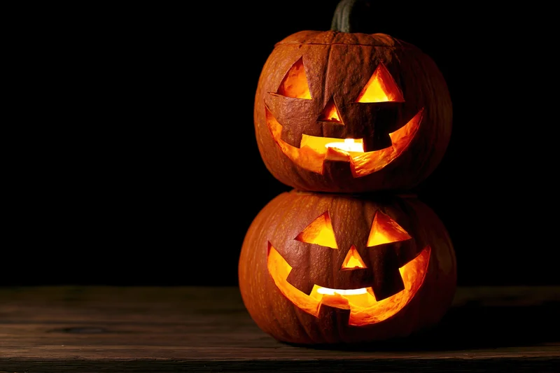 Two carved jack-o-lanterns stacked on a wooden table glowing in the dark