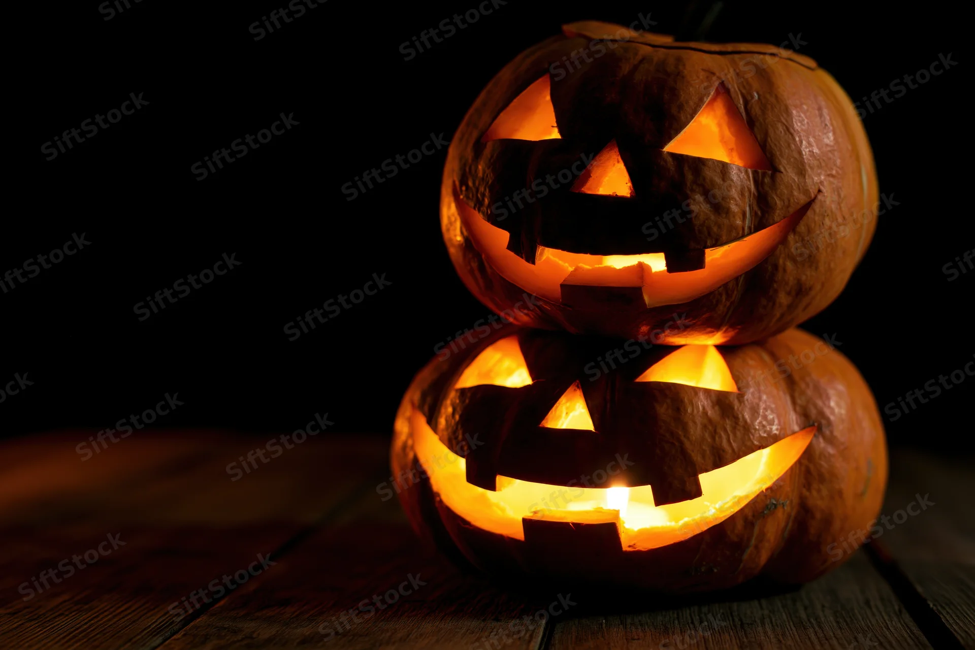 Two carved jack-o-lanterns stacked and glowing on a wooden table at night