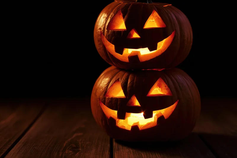 Two carved jack-o-lanterns stacked and glowing on a wooden table at night
