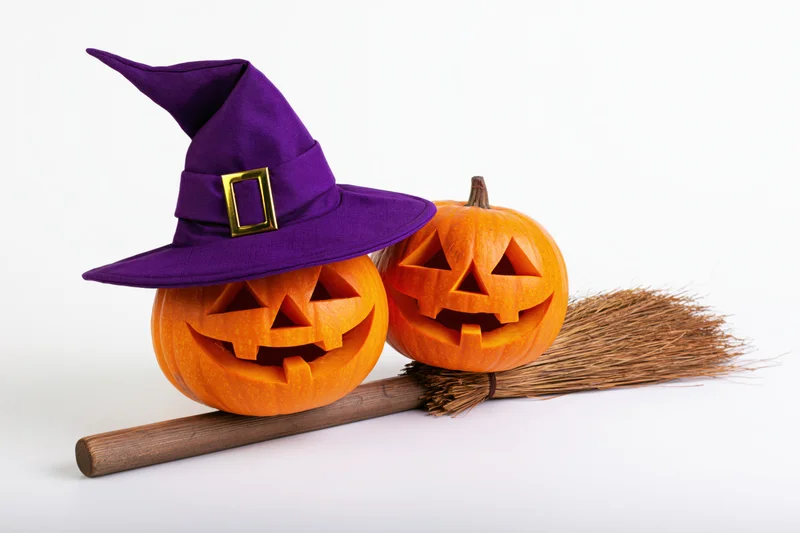 Two carved jack-o-lanterns with a witch hat and broom on white background