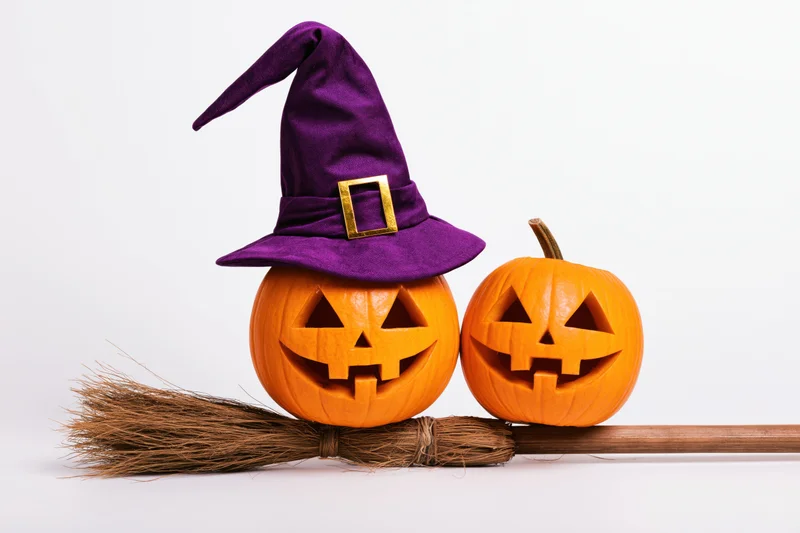 Two carved jack-o-lanterns with a witch hat and broom on white background