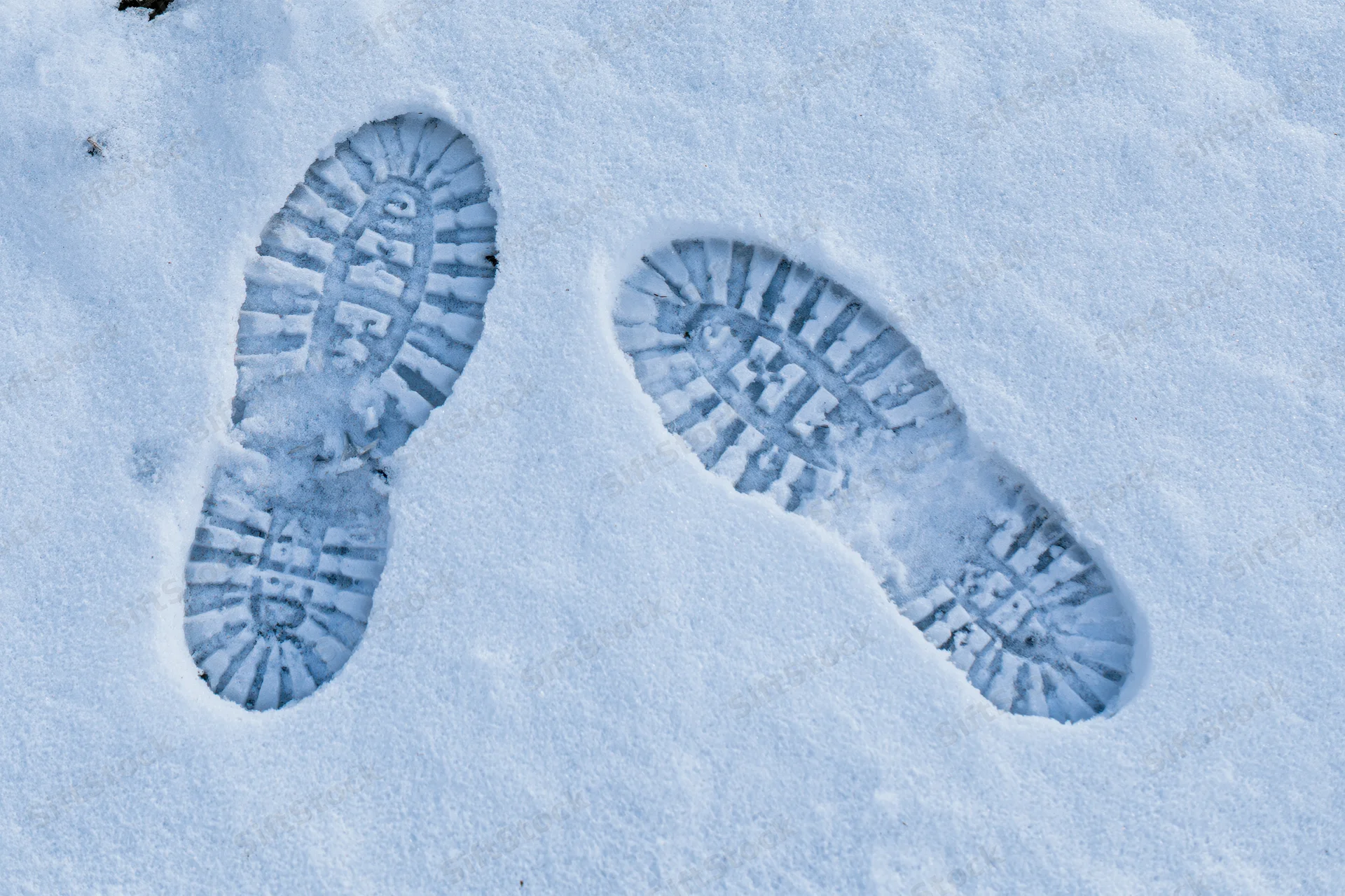 Two deep boot prints pressed into fresh white snow showing tread pattern