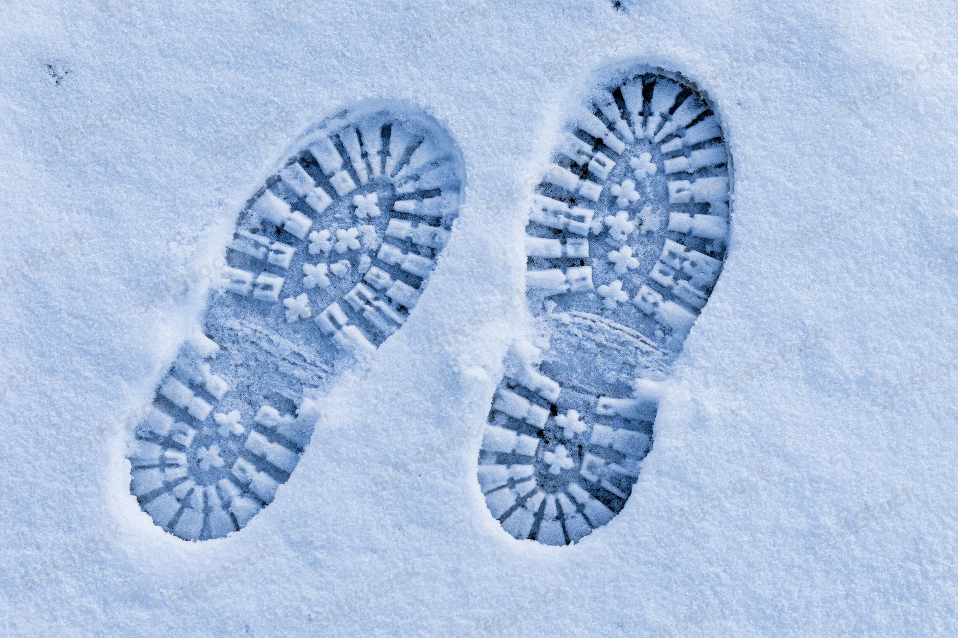 Two deep boot prints pressed into fresh snow showing detailed tread pattern