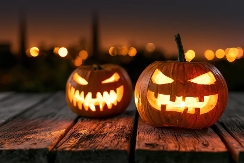 Two glowing jack-o-lanterns with carved grimacing faces on a wooden table at twilight