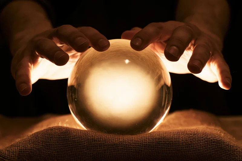 Hands curving around a glowing crystal ball resting on burlap fabric in dim light