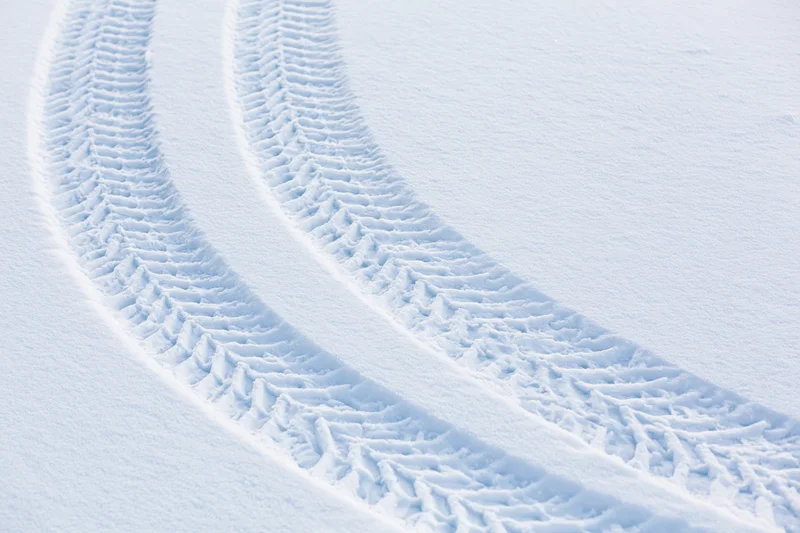 Two parallel tire tracks curving through fresh snow in a winter landscape