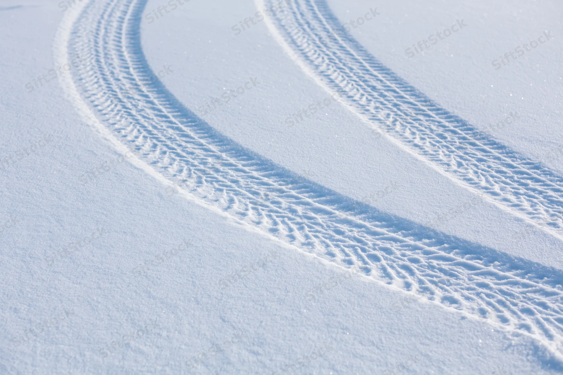 Parallel tire tracks curving through fresh snow on a smooth winter landscape