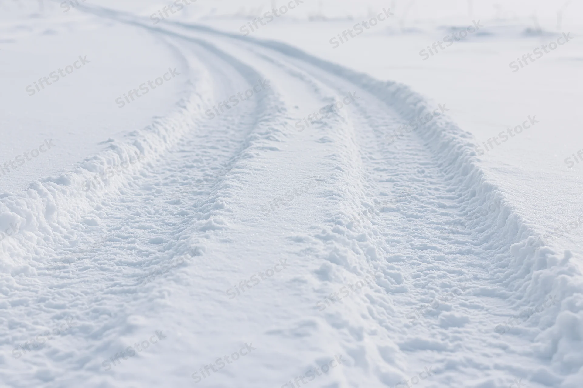 Parallel tire tracks curving through snow-covered rural landscape