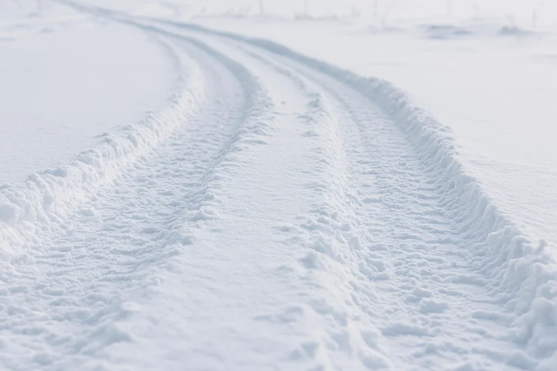 Parallel tire tracks curving through snow-covered rural landscape