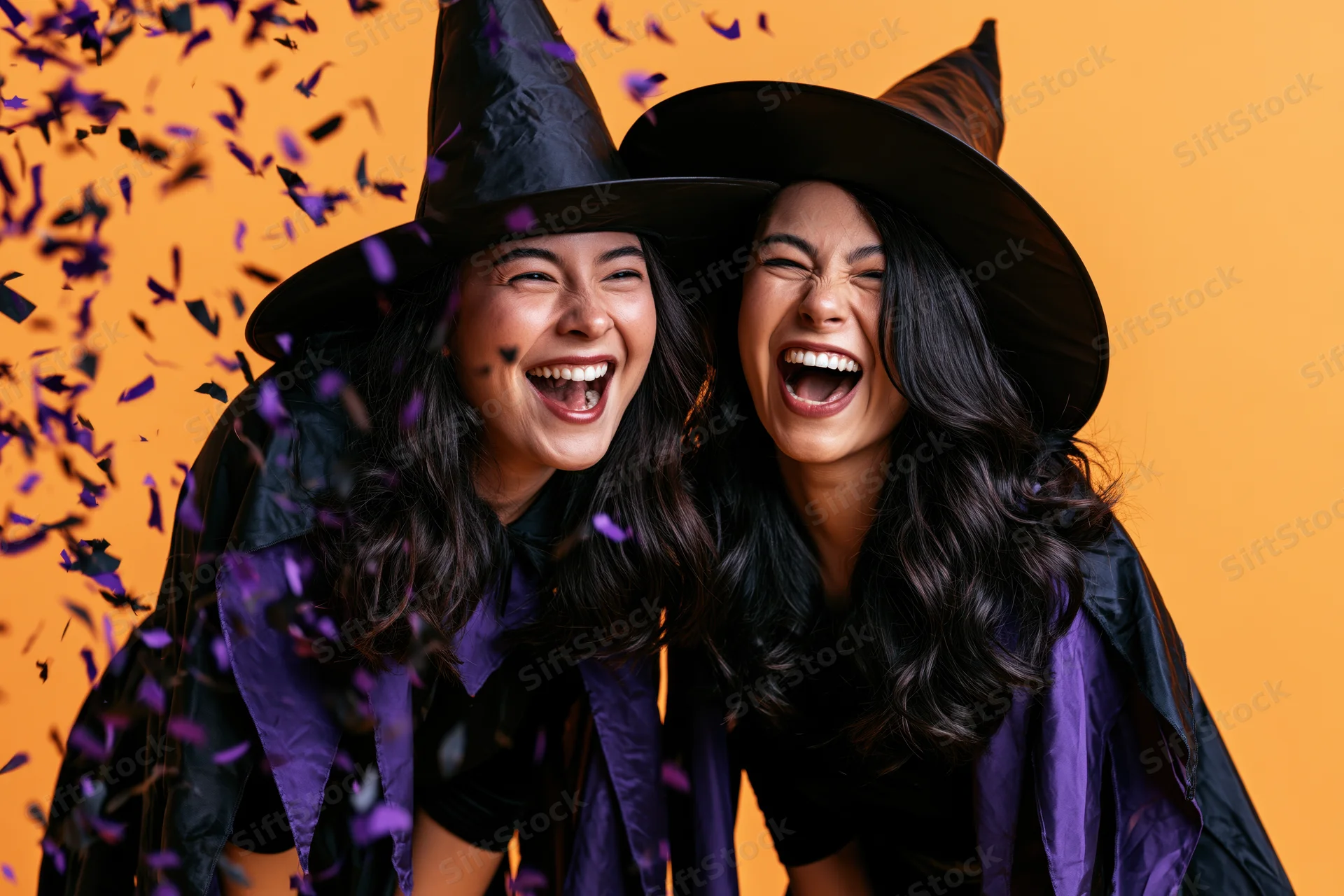 Two young women in witch costumes laughing together at a halloween party