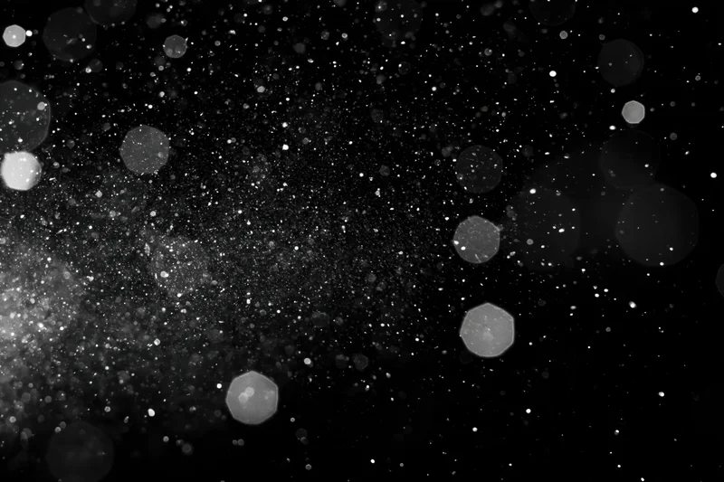 Water droplets and dust particles suspended in midair against a black background with bokeh light effects