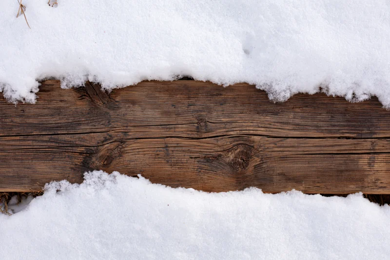 Weathered wooden plank partially covered in snow lying flat outdoors