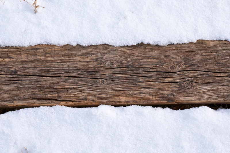 Weathered wooden plank lying flat outdoors partially buried in snow