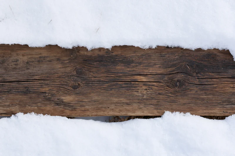 Weathered wooden plank lying flat outdoors partially buried in snow