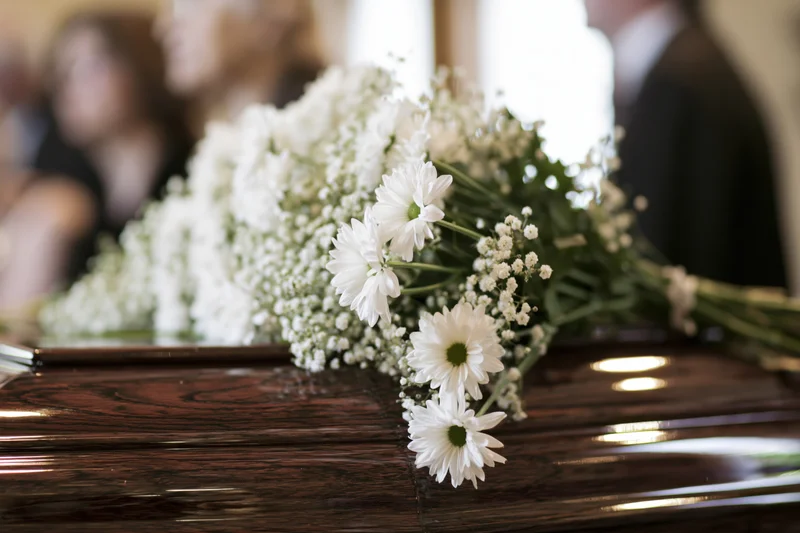 White daisies and baby's breath arranged on polished wooden coffin at funeral service