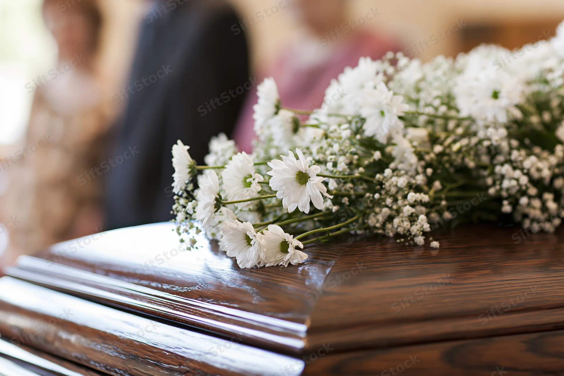 White daisies and baby's breath arranged on polished wooden coffin lid at funeral service