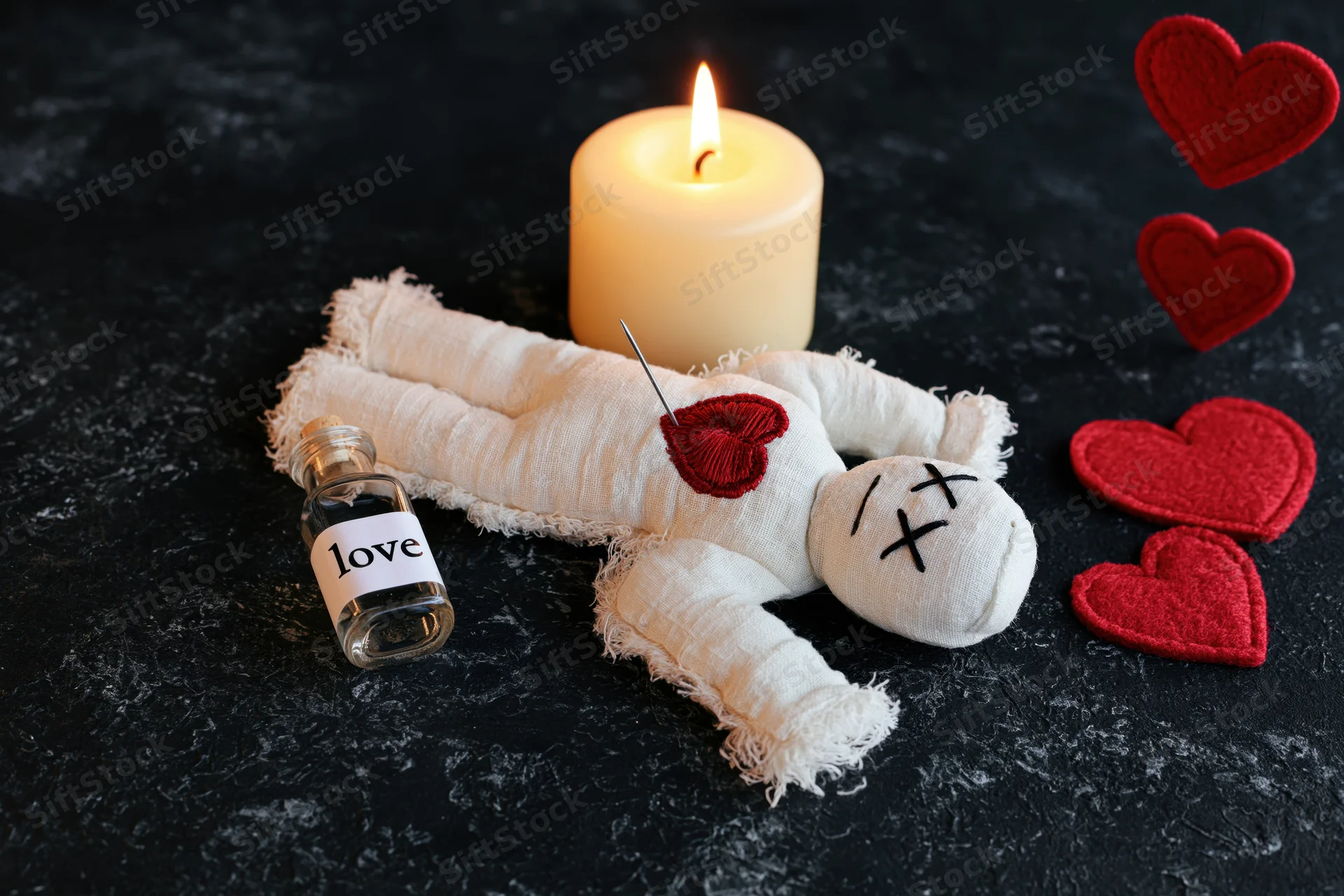 White fabric voodoo doll lying flat on dark surface with red hearts, lit candle, and bottle labeled love