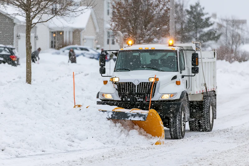 White municipal snowplow truck clearing snow from residential street during snowfall