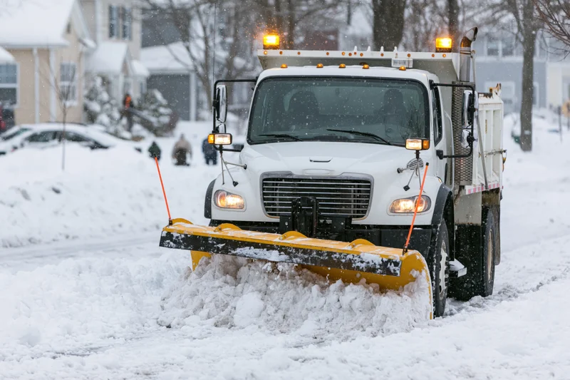 White municipal snowplow truck clearing snow from residential street during snowstorm