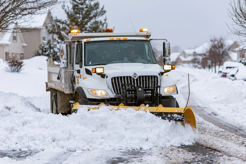 White municipal snowplow truck clearing snow from residential street in winter