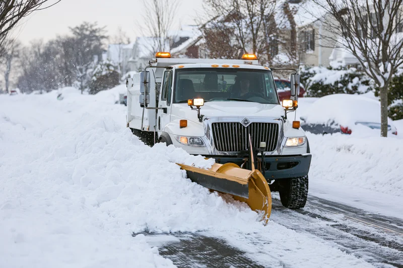 White municipal snowplow truck clearing snow from residential street during snowfall