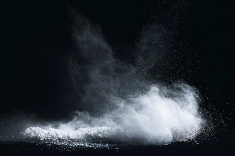 White powder exploding midair against a pure black studio background