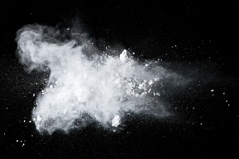 White powder exploding mid-air in a horizontal burst against black background