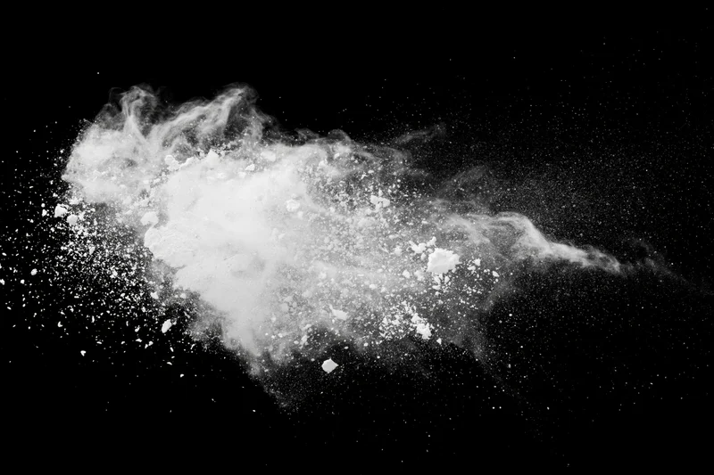 White powder exploding mid-air in a horizontal burst against black background