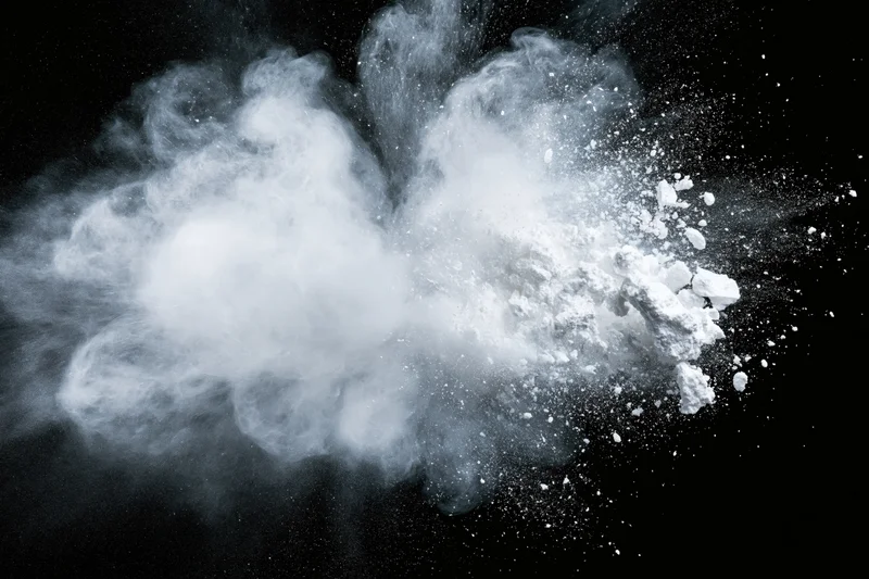 White powder exploding midair in a wide horizontal burst against black background