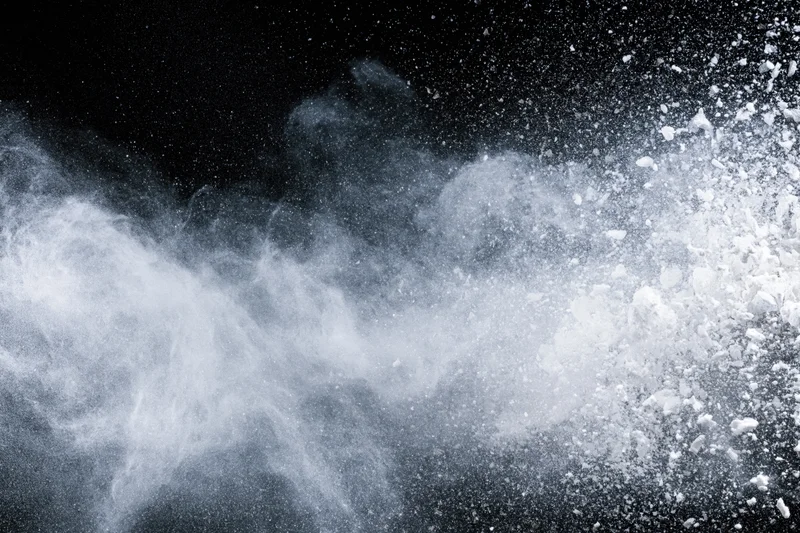 White powder exploding mid-air in a wide horizontal burst against black background
