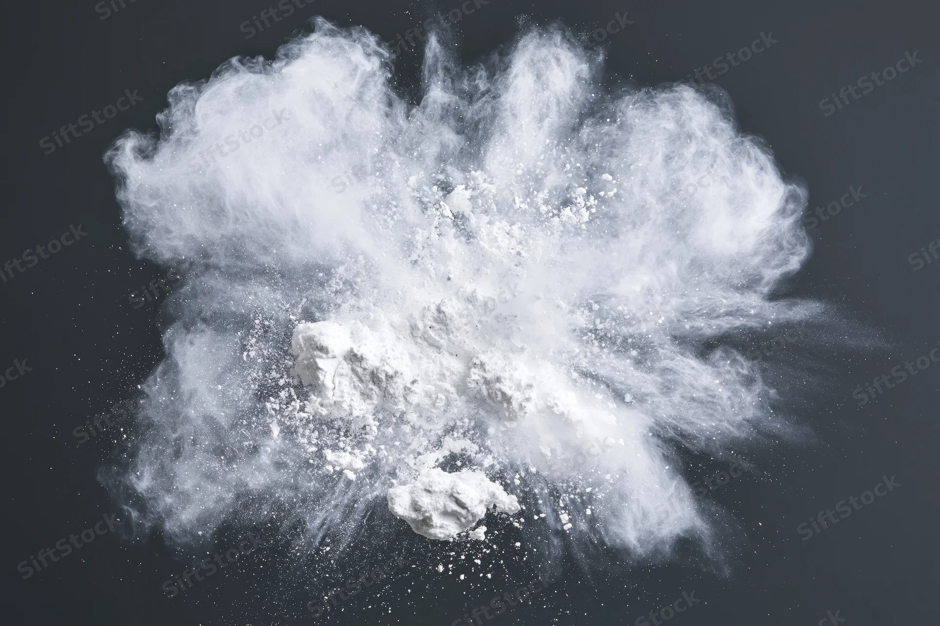 White powder exploding midair with particles scattering outward against dark background