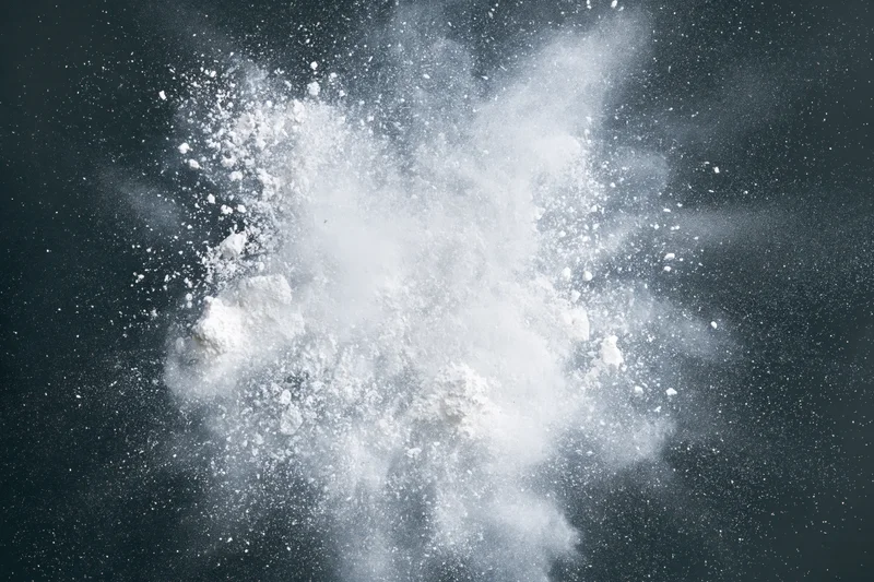 White powder exploding midair with particles scattering outward against dark background