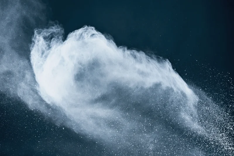 White powder exploding in mid-air forming a sweeping arc against a dark background