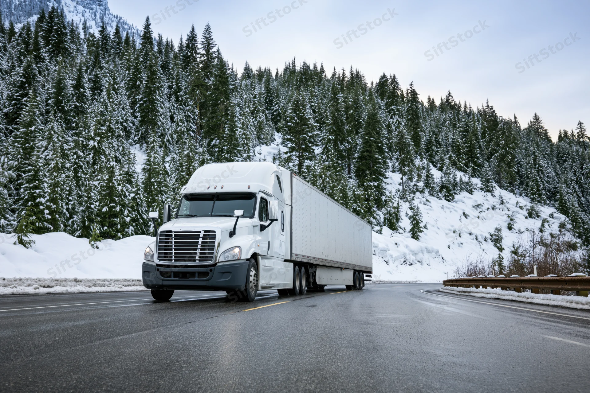 White semi-truck with refrigerated trailer driving on wet mountain road in winter forest