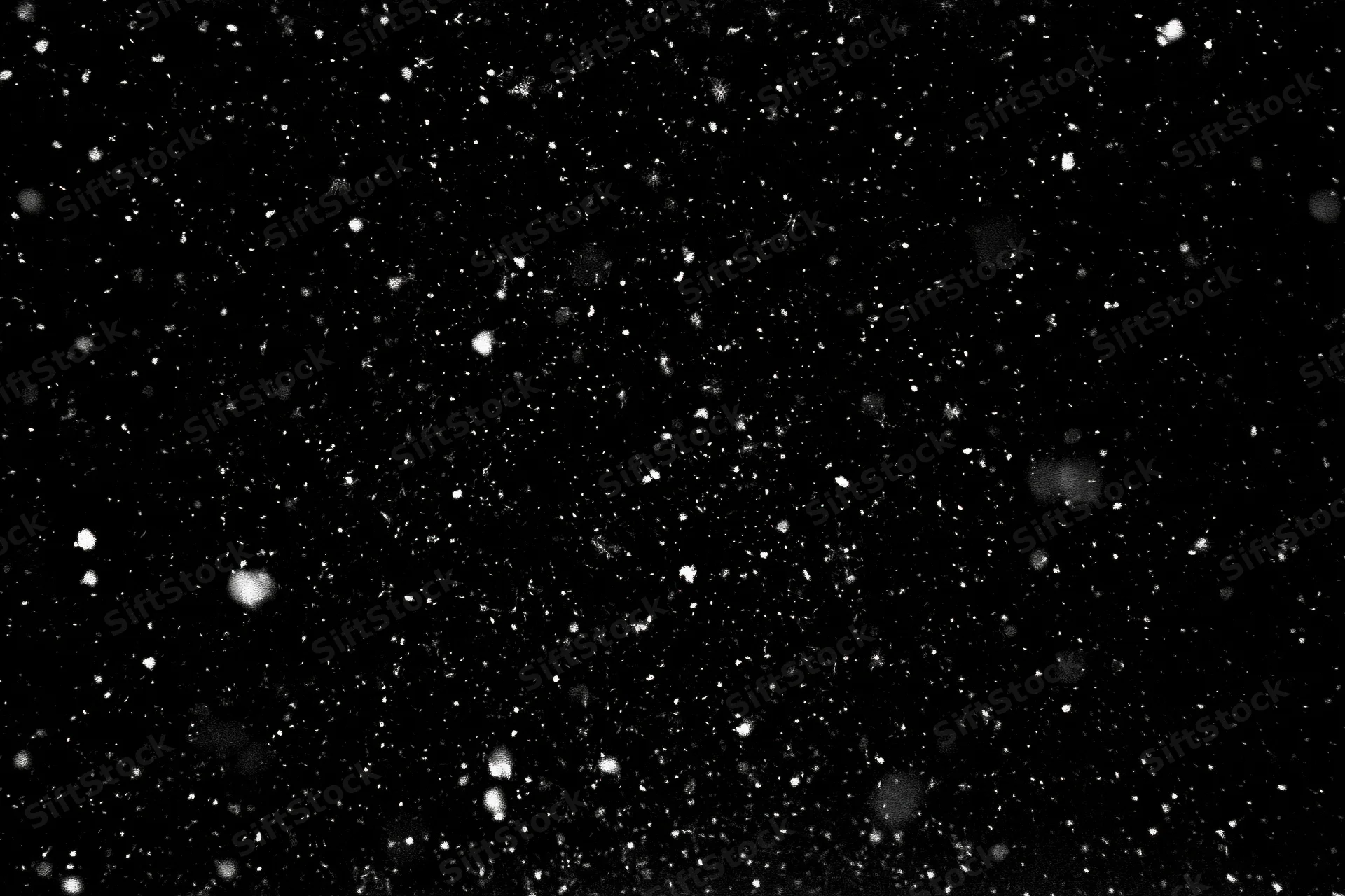White snow particles and small snowflakes falling against a black background