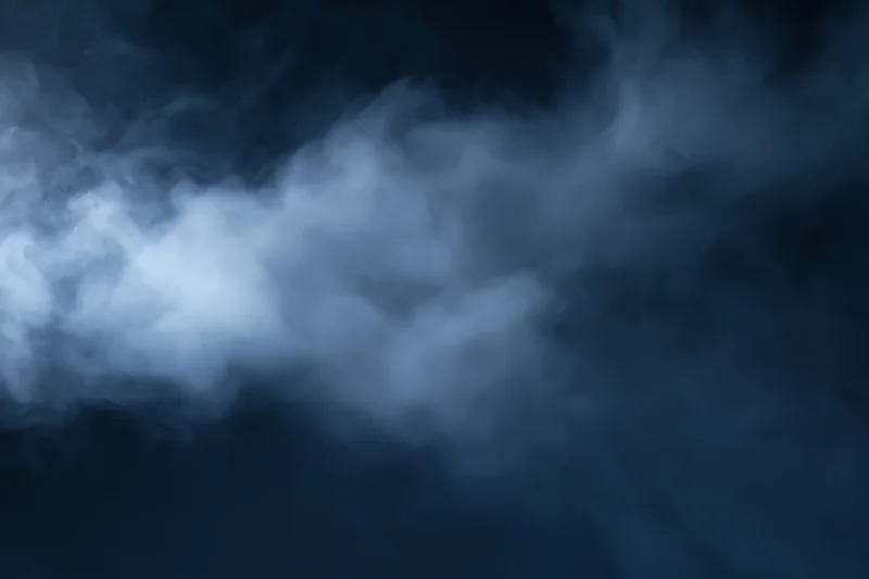 Wispy white smoke drifting through dark air
