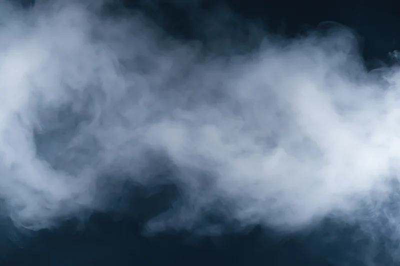 Wispy white smoke drifting through dark air