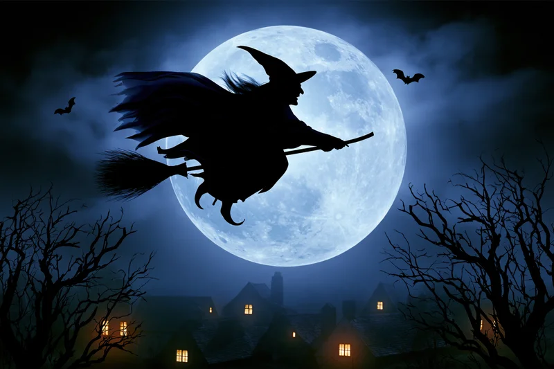 Witch silhouette flying on broomstick across full moon over village at night
