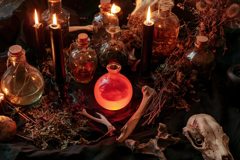 Witchcraft altar with candles, bottles, herbs and bones arranged on black cloth