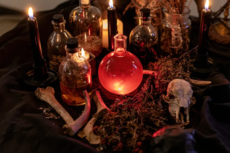 Witchcraft altar with candles, glass bottles, skull and herbs arranged on black cloth