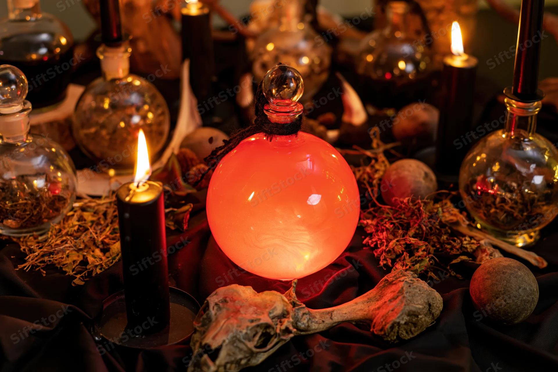 Witchcraft altar with candles, potion bottles, bones and herbs arranged on black cloth