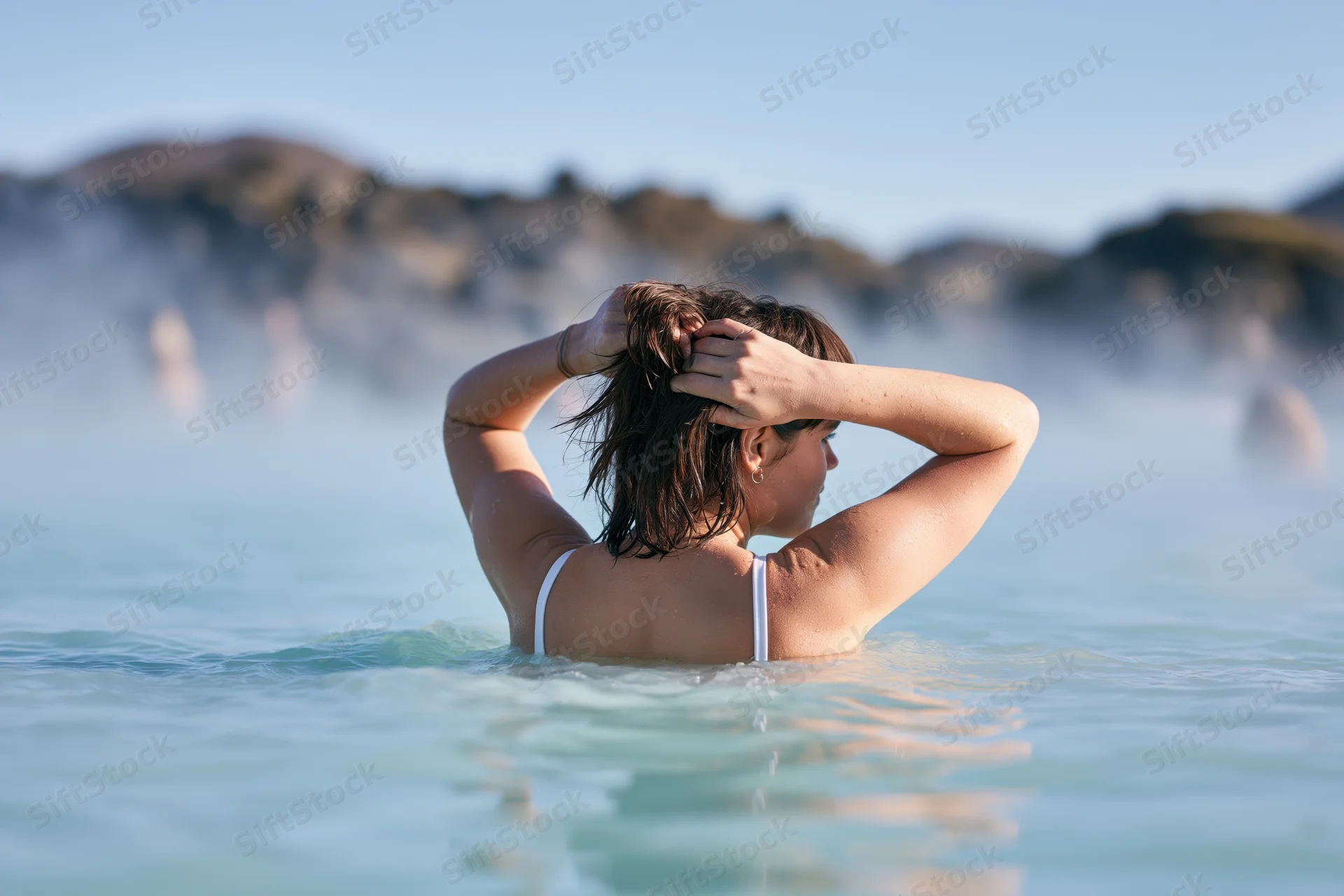Woman from behind in a steaming geothermal pool with hands in her wet hair