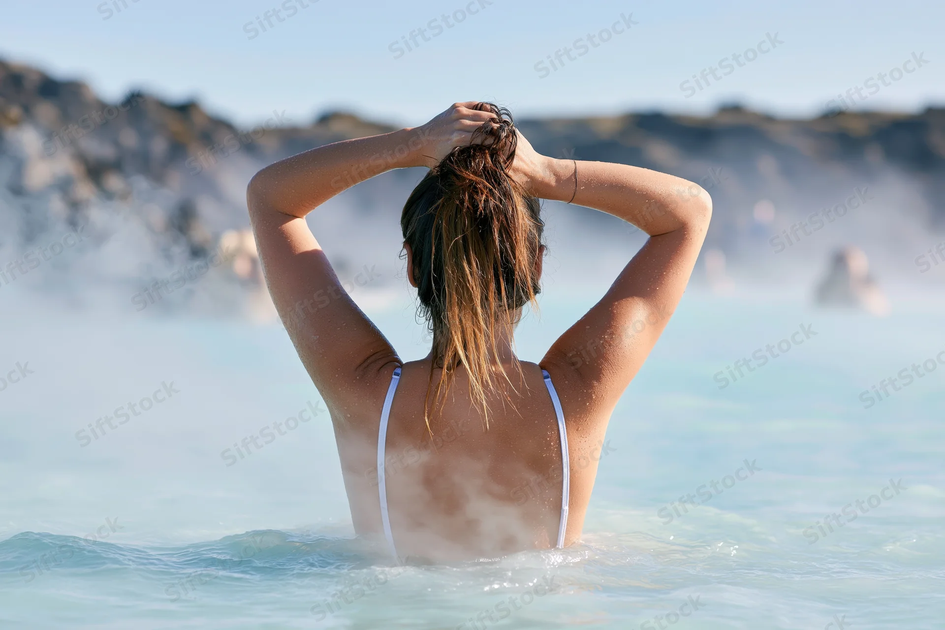 Woman from behind in a steaming geothermal pool with hands in her wet hair