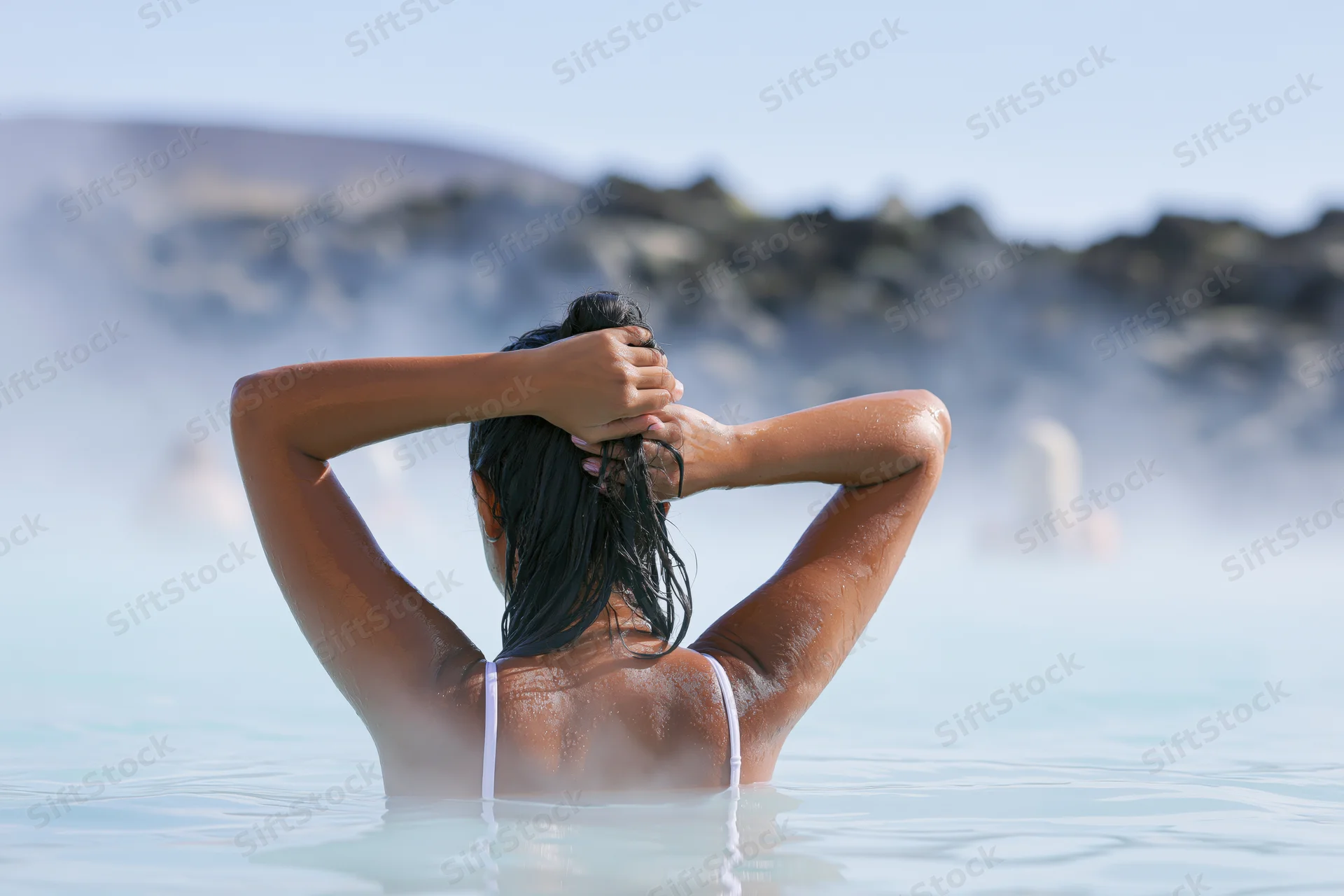 Woman from behind in a steaming geothermal pool with hands in her wet hair